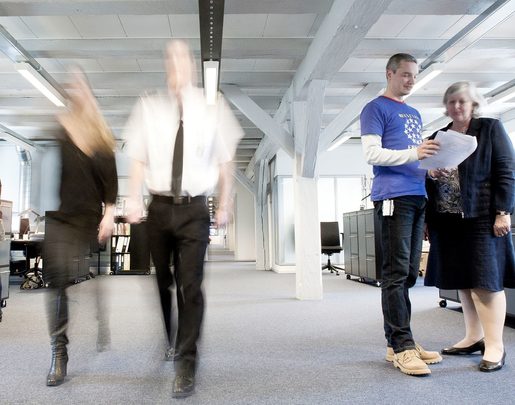 To personer arbejder sammen i et moderne kontormiljø med åbent rum, naturligt lys og synlige bjælker.