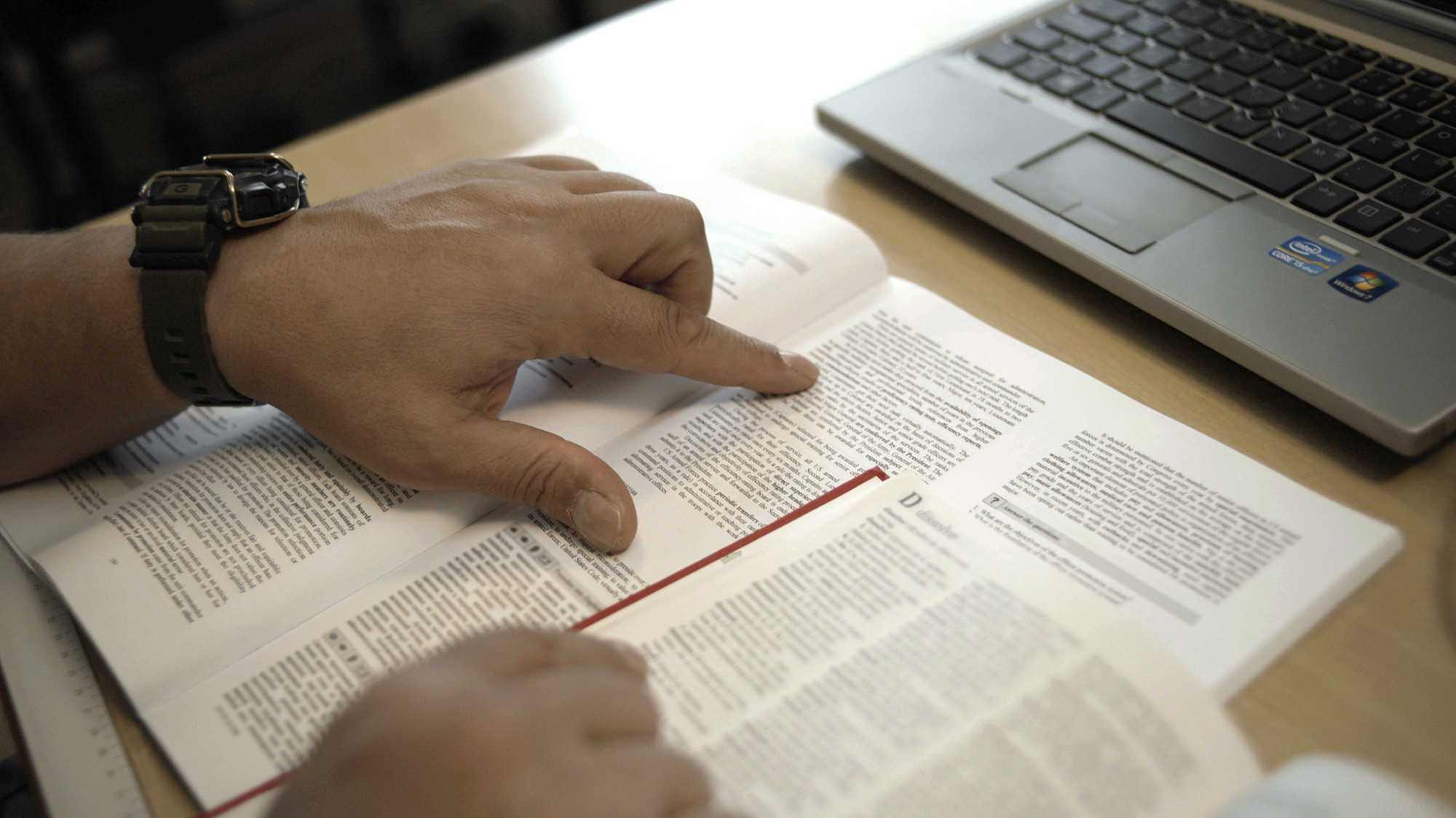 Et billede tæt på af et menneske der sidder og læser en bog. Bogen ligger på et bord og personen læner sig henover bogen