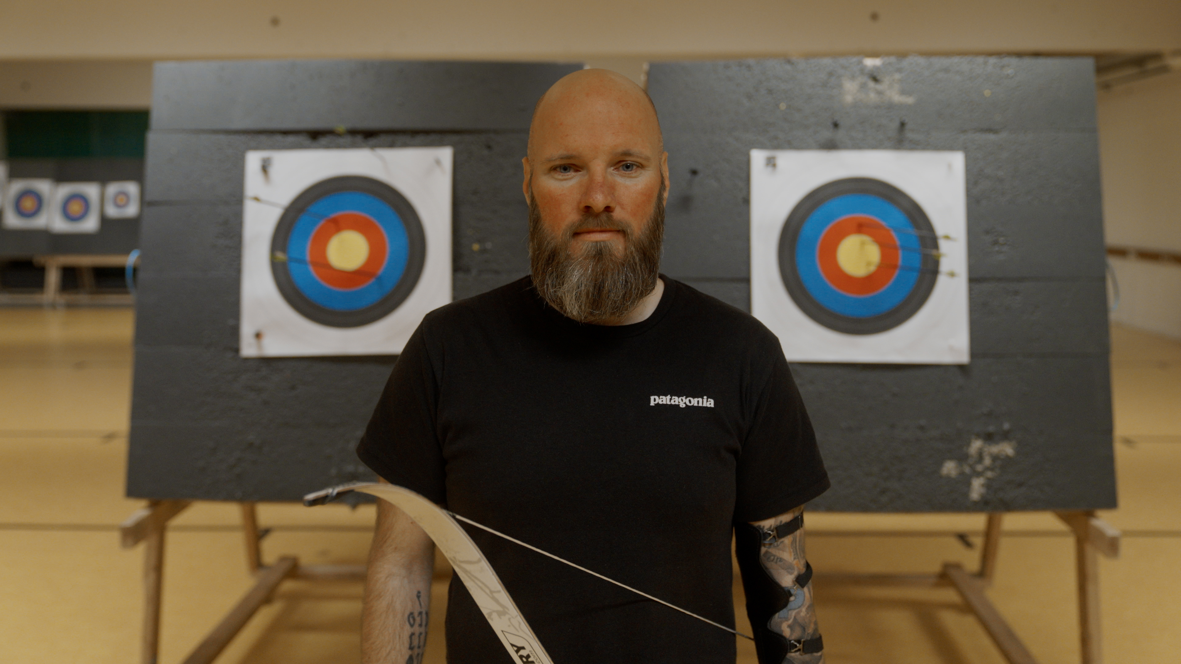 Veteranen Dennis står med to målskiver i baggrunden. I hånden holder han bue.