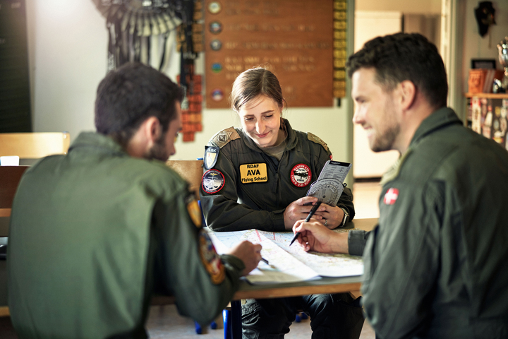 Kvindelig pilot sidder ved bord med to andre