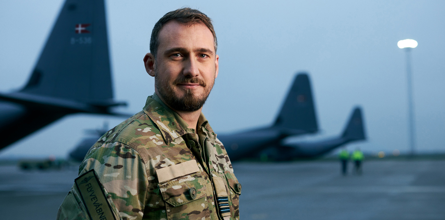 Teknikofficer Kasper står med 3 Hercules transportfly i baggrunden