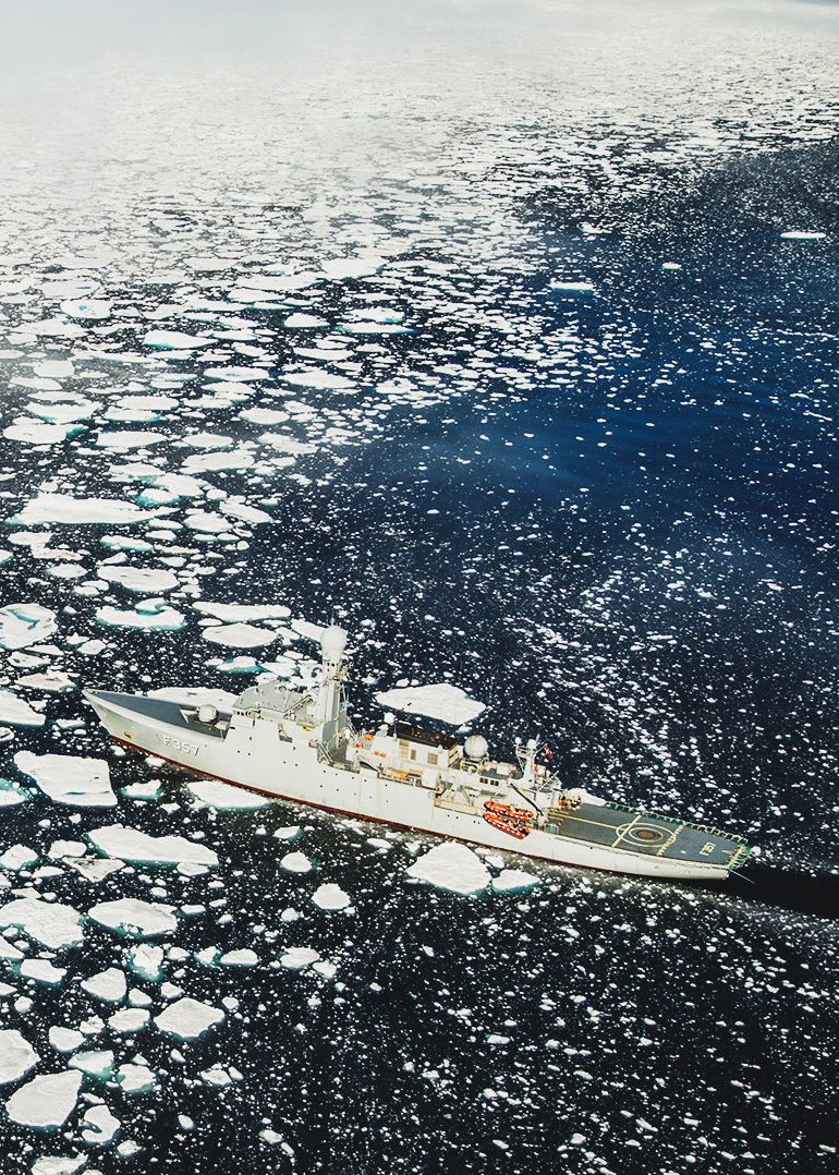 Militærskib sejler gennem isfyldt hav med isbjerge og åbent vand under barske polare forhold.