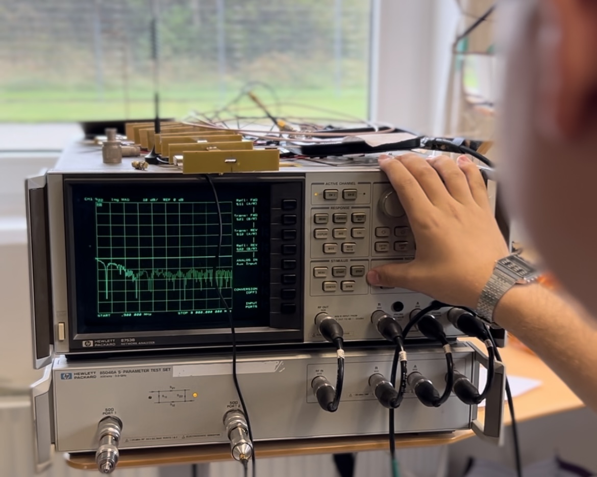 Elektronikfagtekniker tester avanceret måleudstyr i laboratorie med HP-netværksanalysator og signalkabler tilsluttet.