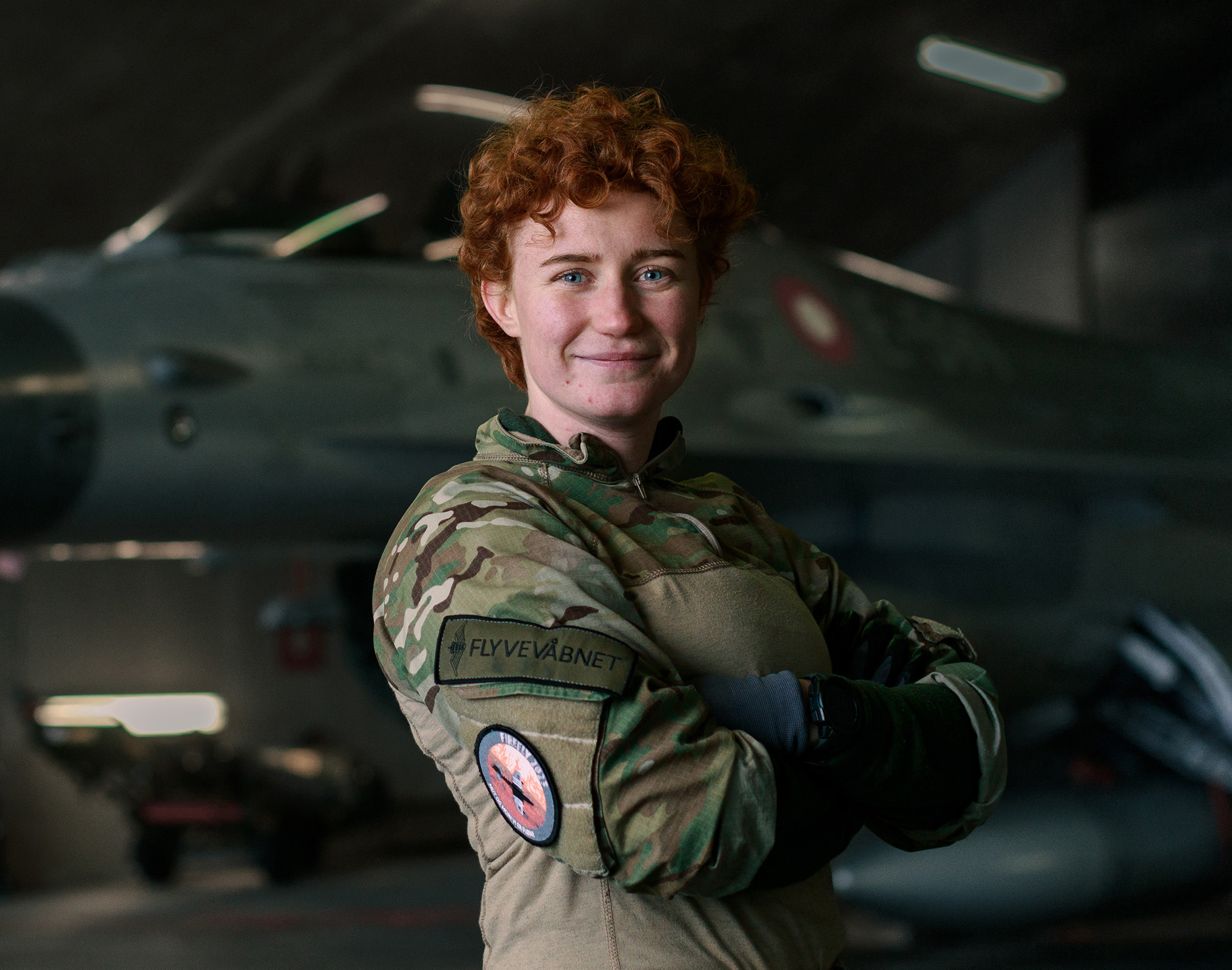 Person i Flyvevåbnets uniform står i en hangar foran et kampfly med armene over kors.