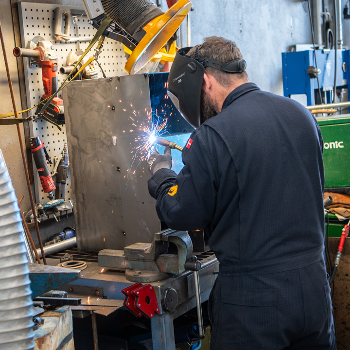 Våbenmekaniker i svejser på en metalplade på et værksted