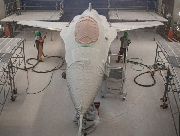 to mand i beskyttelsesdragter er ved at overfladebehandle F16