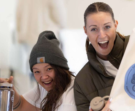 To kvinder griner og holder drikkedunke og merchandise fra FFK-netværket.