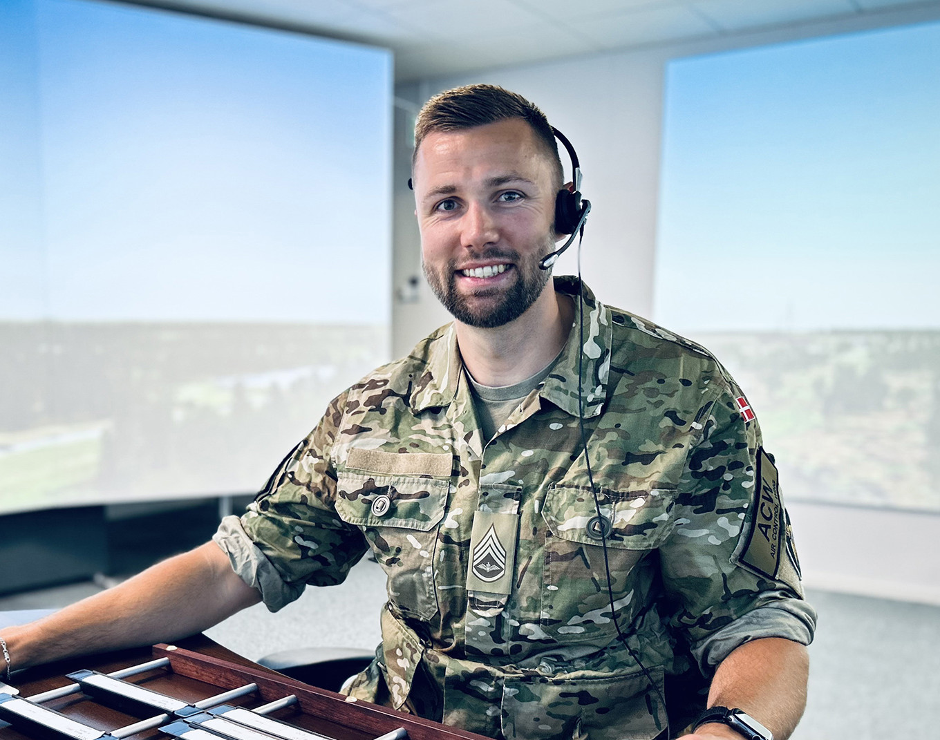 En uniformeret medarbejder med headset sidder ved en arbejdsstation i et kontrolmiljø.