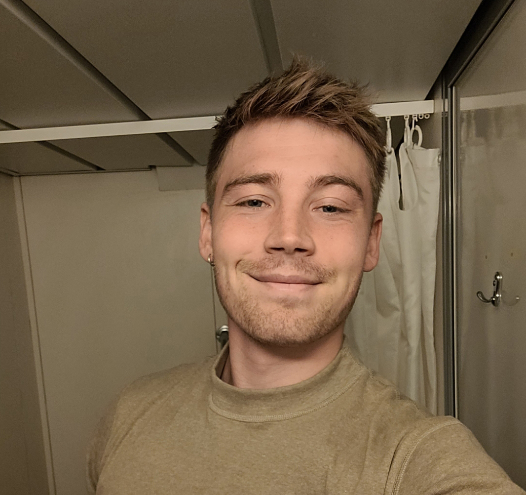 Ung person i uniform står i et lille rum og smiler til kameraet.