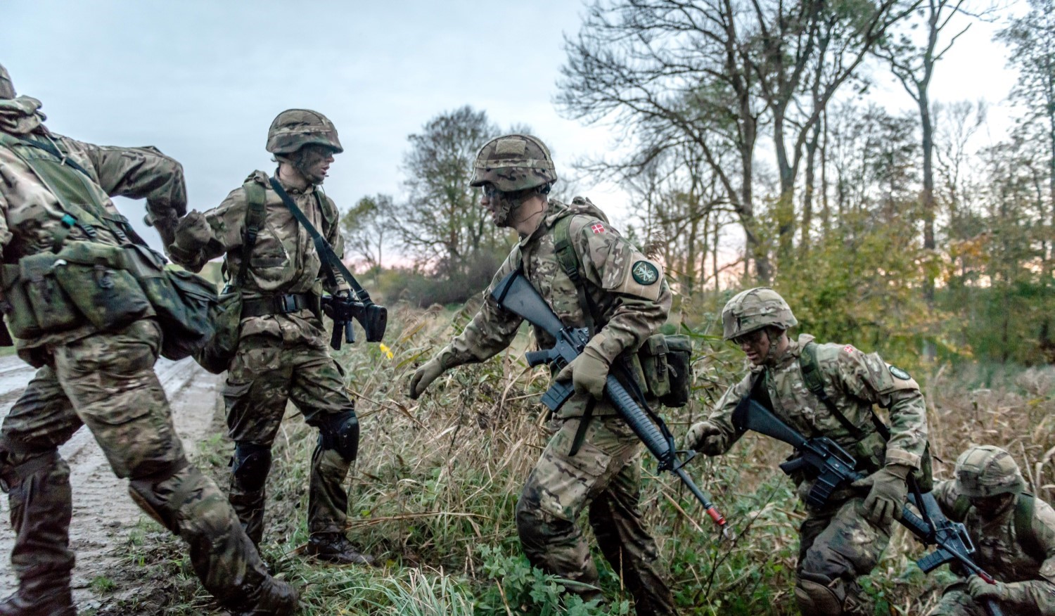 Grupper af soldater i camouflage hjælper hinanden op af grøft