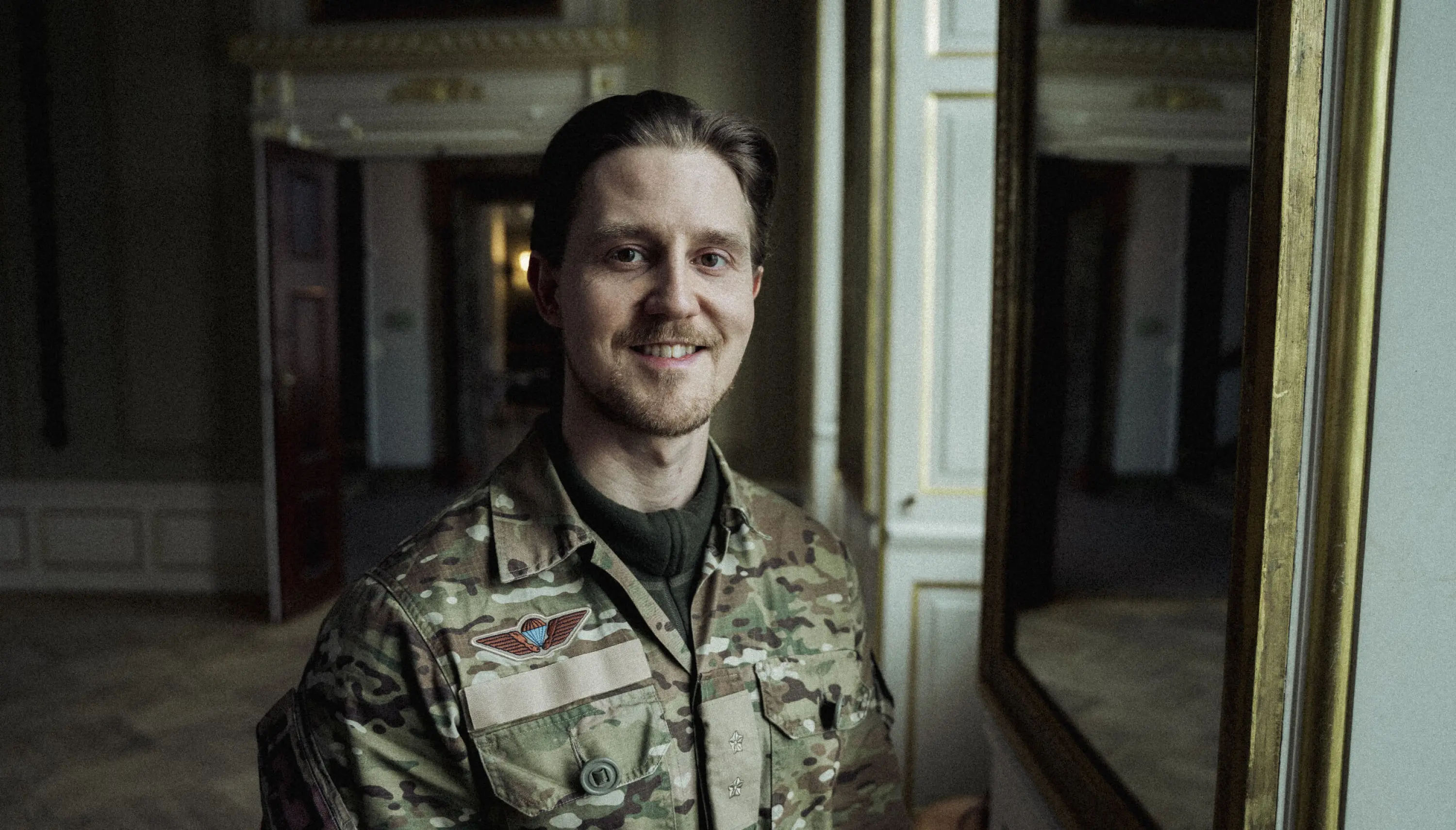 Lasse står i Frederiksberg slot i sin uniform og smiler til kameraet