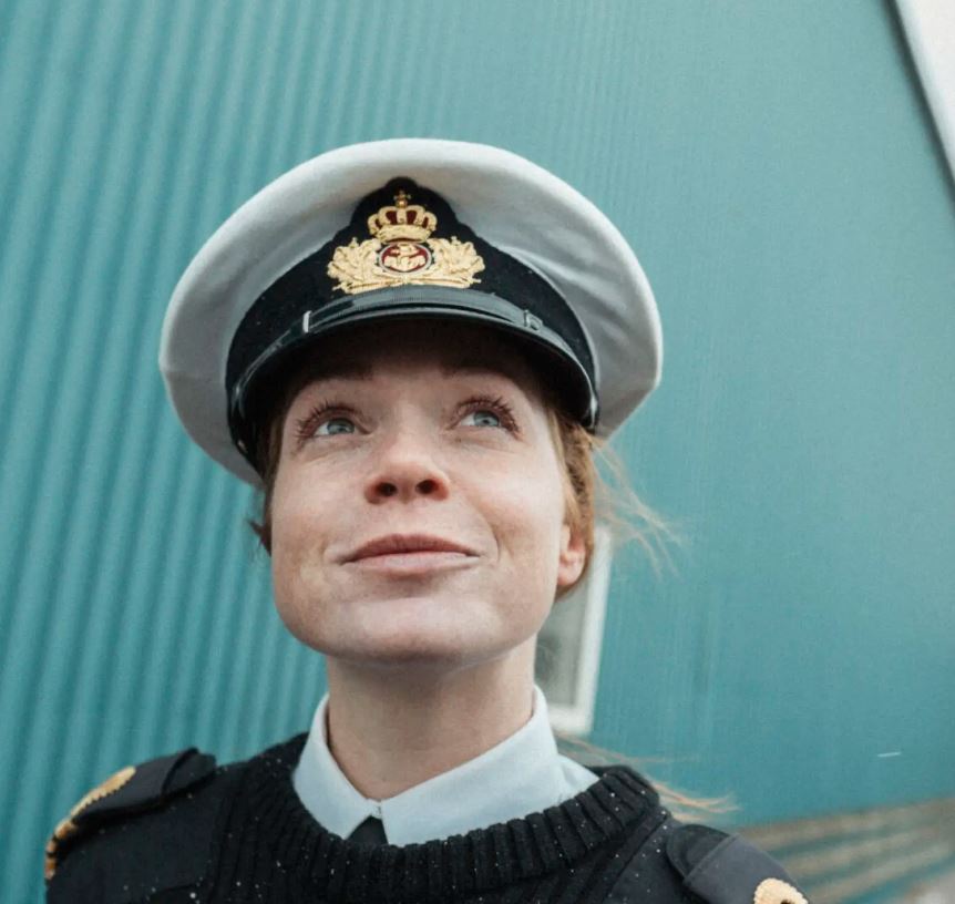 Skibchef Lykke kigger drømmende op over kameraet, med industrielle bygninger bag sig