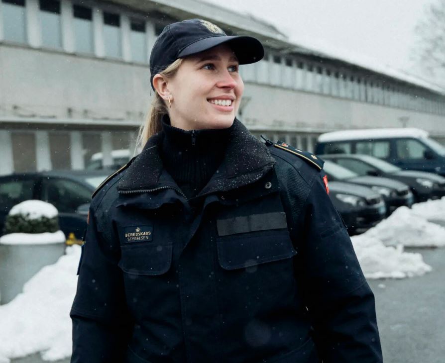 Pernille står i sin uniform glad og smilende foran sin arbejdsplads