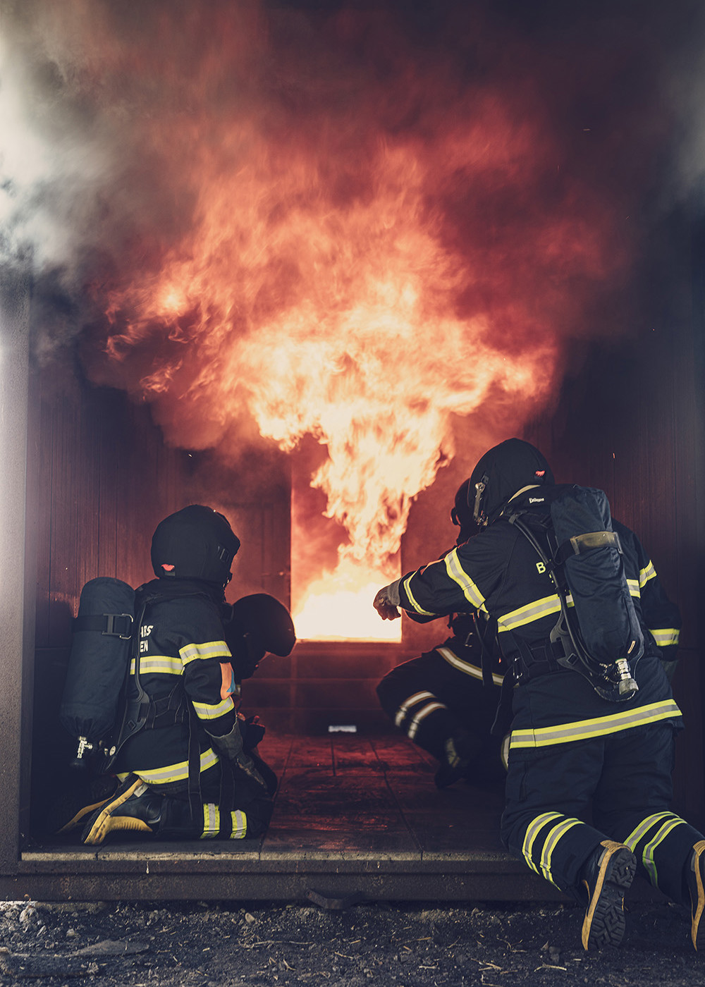 Brandmænd i indsatsdragter træner indendørs brandbekæmpelse foran en voldsom flammeudvikling under kontrolleret brandøvelse.