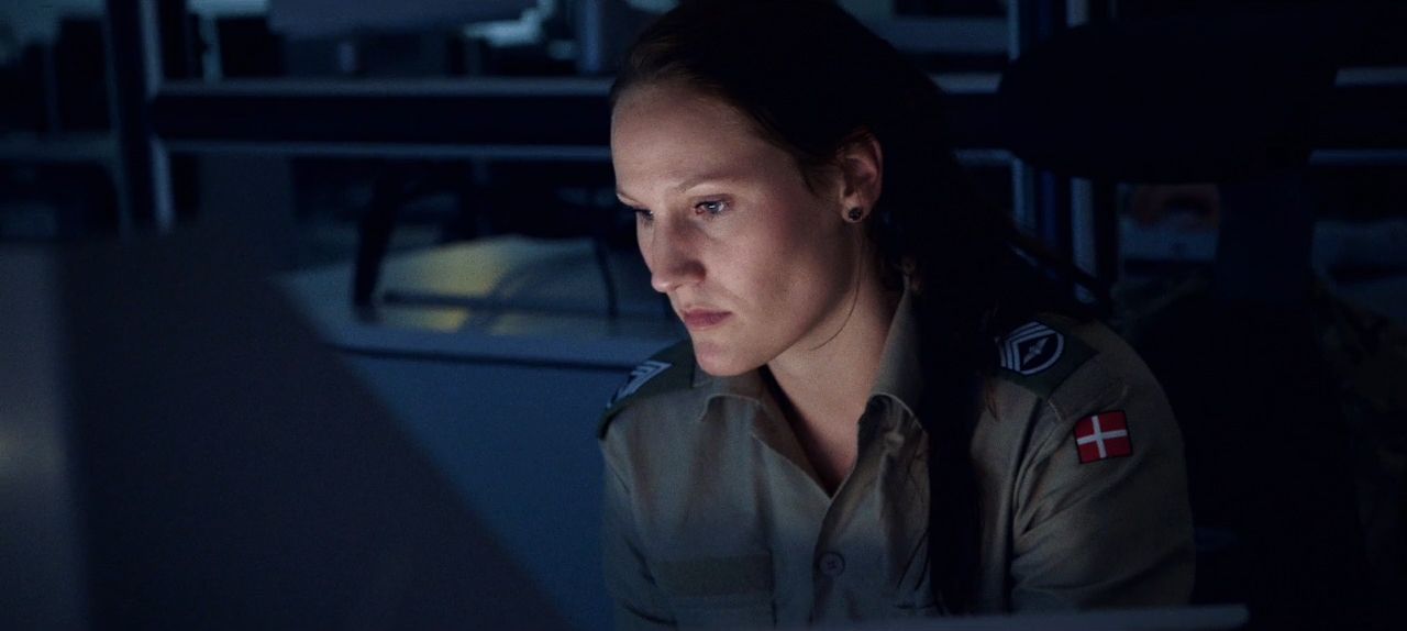 Kvindeligt sergent sidder med front mod skærm i mørkt rum