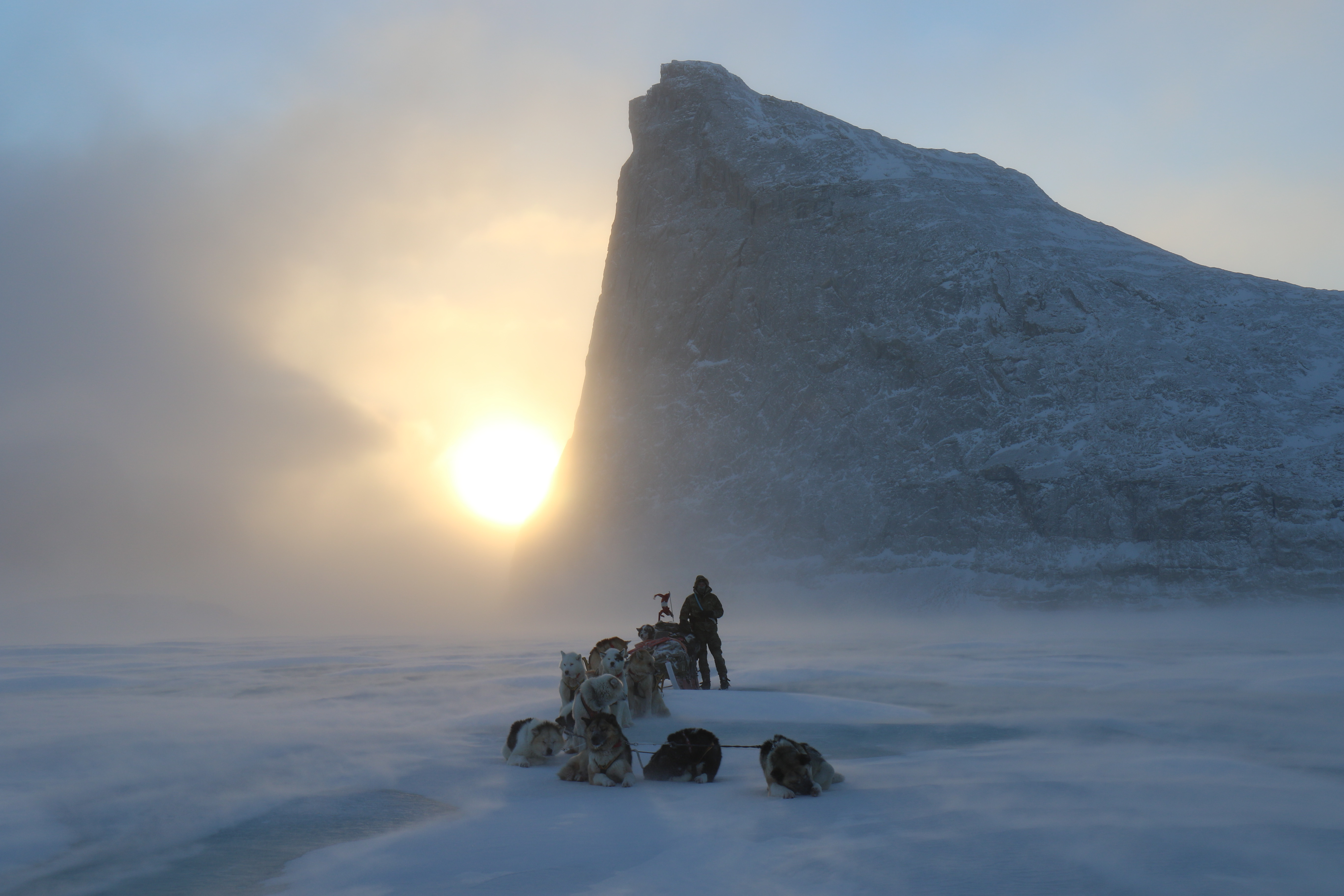 Hundeslæde på sneen foran et stort bjerg i tåget sollys.