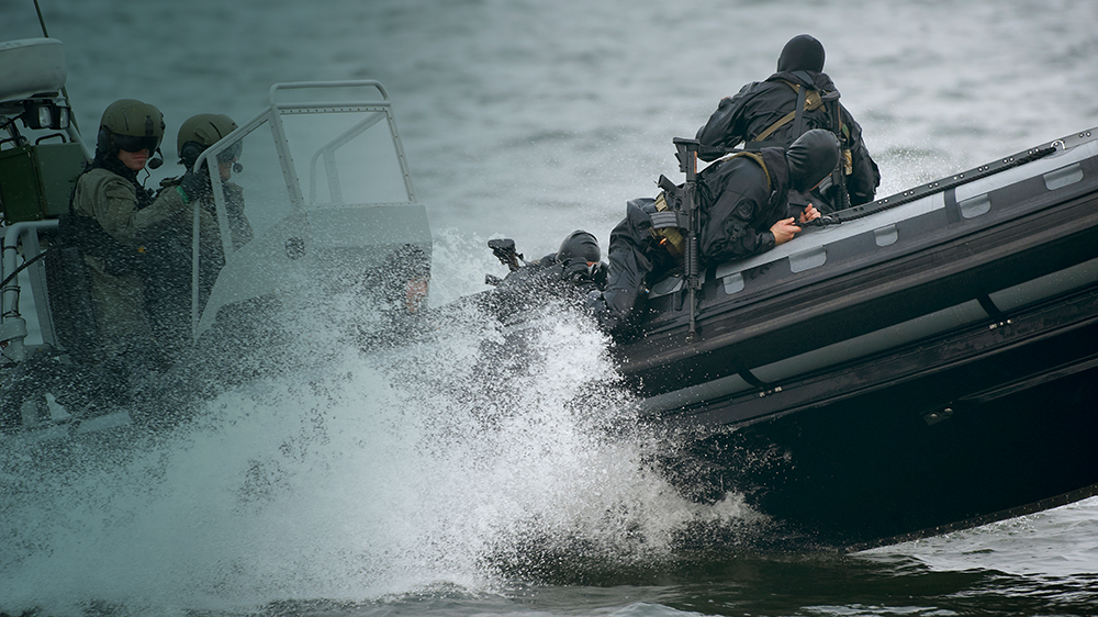 Specialstyrker i sort uniform læner sig ud fra siden af en hurtiggående båd under en taktisk øvelse