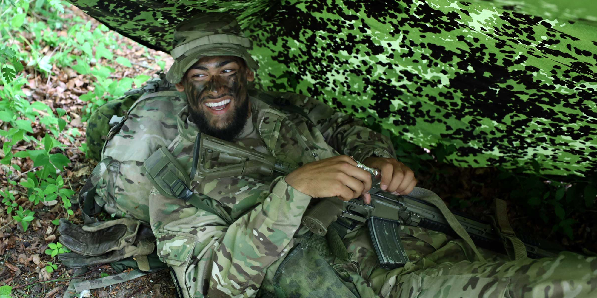 Soldater ligge under camouflage teltdug
