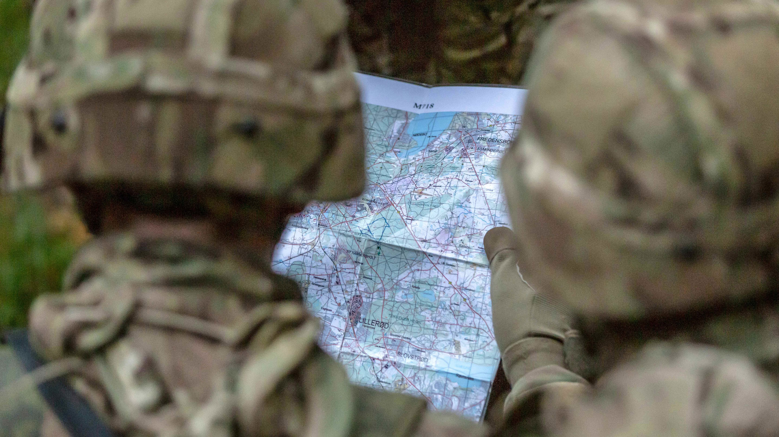 To soldater i camouflageuniform studerer et detaljeret kort sammen ude i terrænet.